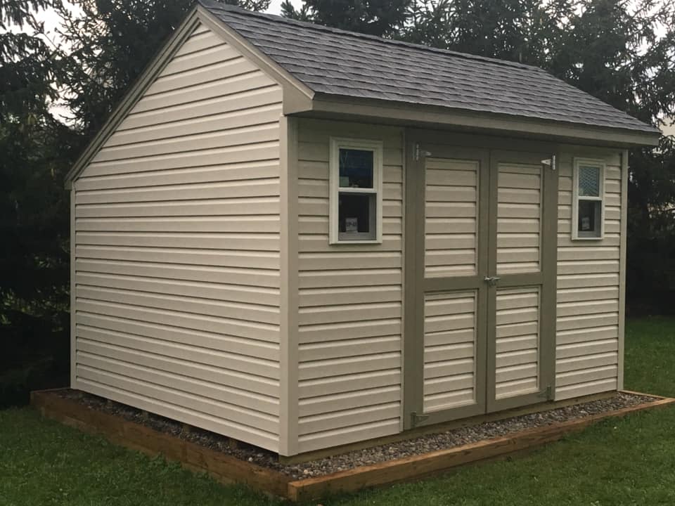 Tan shed with dark gray roof, two windows, and olive green trim on the doors.