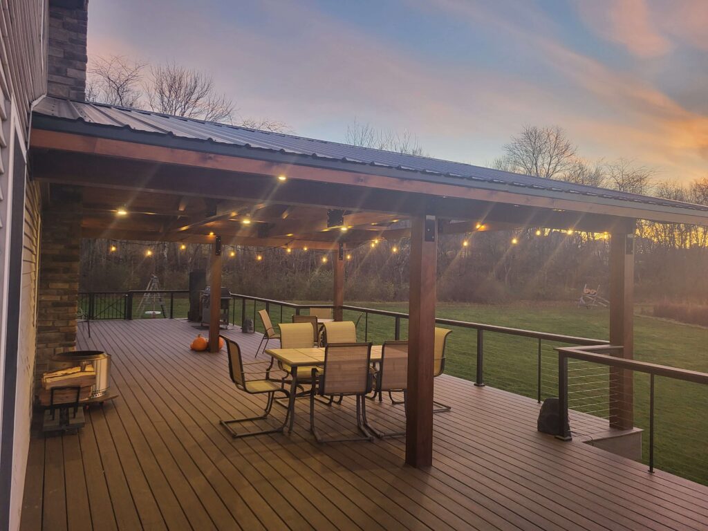 Newly built deck with covering featuring lit Edison lights at sunset.